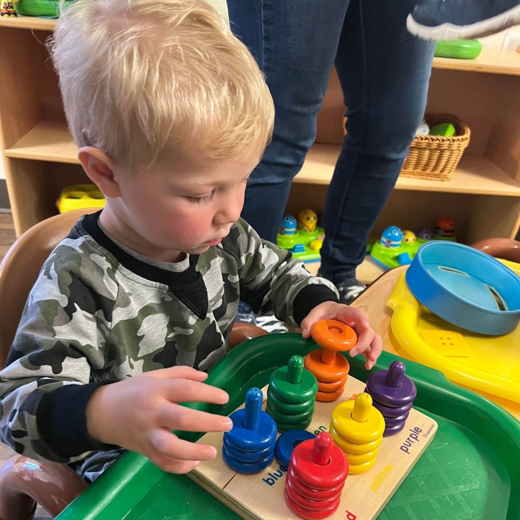 A toddler sorts wooden rings by color in a childcare program at Josie's Learning Center in Stanwood, WA.